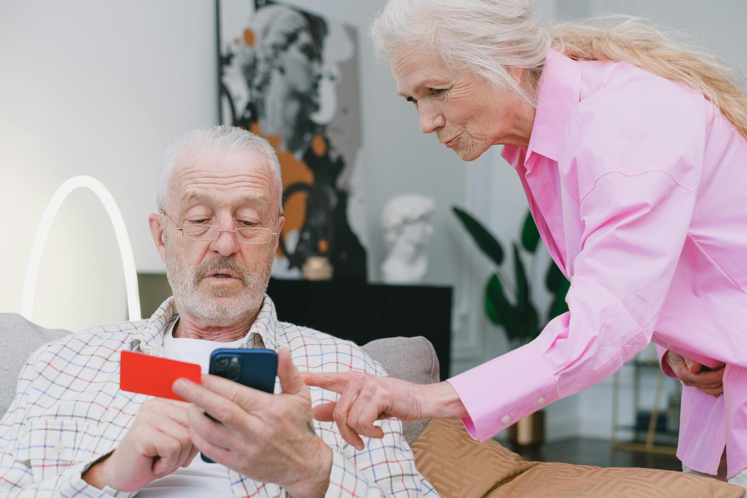 Senior man holding a credit card and smartphone while a caregiver assists him, highlighting the importance of reliable personal hygiene care services for seniors.